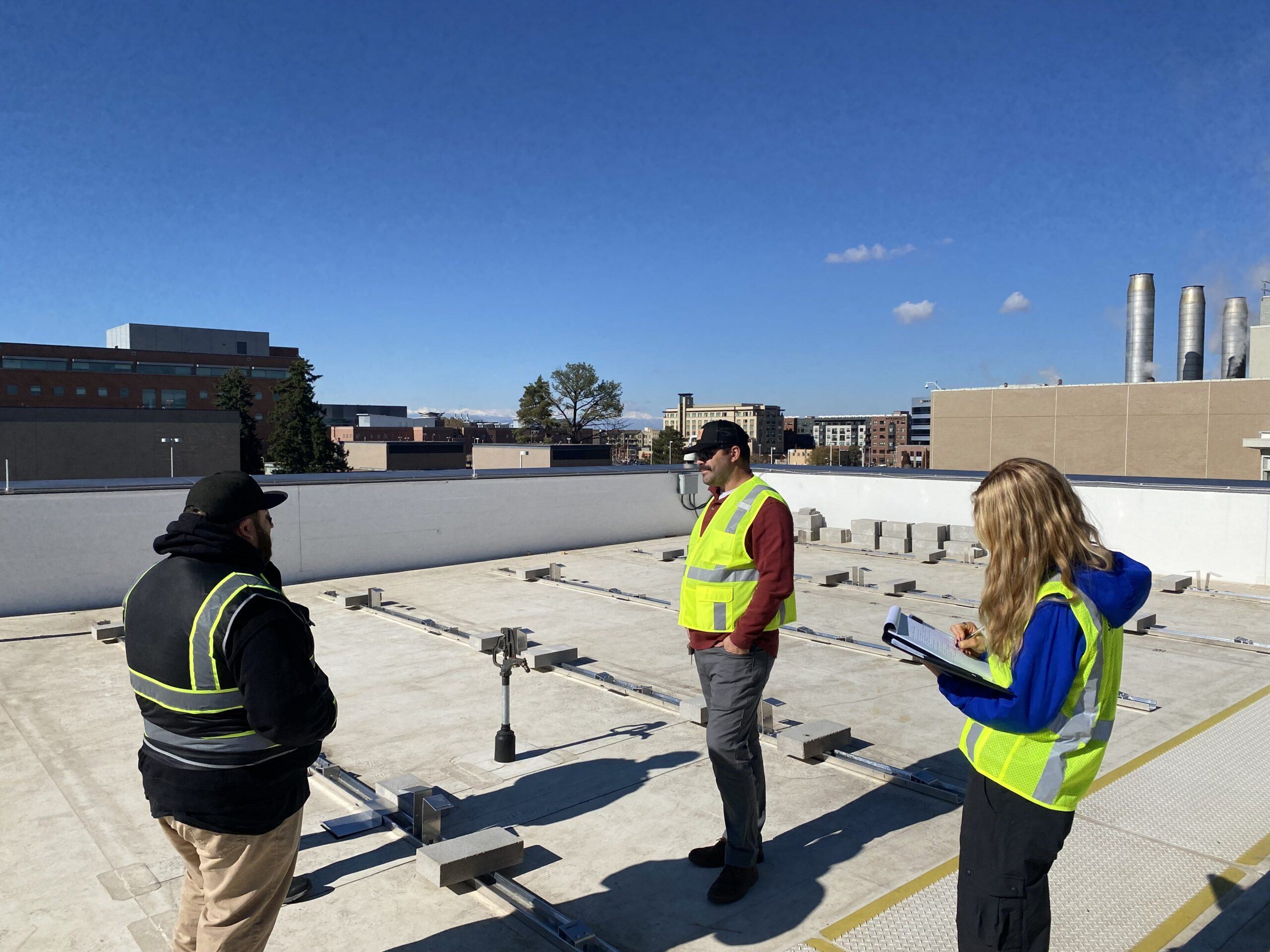 Three people in safety vests standing on a roof, working on the building's energy transition